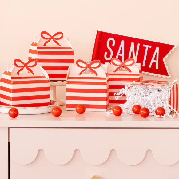 Multiple assembled holiday treat boxes arranged on a pink scalloped cabinet with a "SANTA" banner.