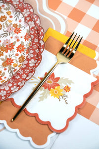 Scalloped fall napkin layered over rust and marigold napkins next to stacked floral paper plates