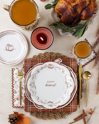 Happy Harvest paper plates layered on autumn plaid square plates with fall napkins, roasted turkey, and seasonal Thanksgiving table decor.