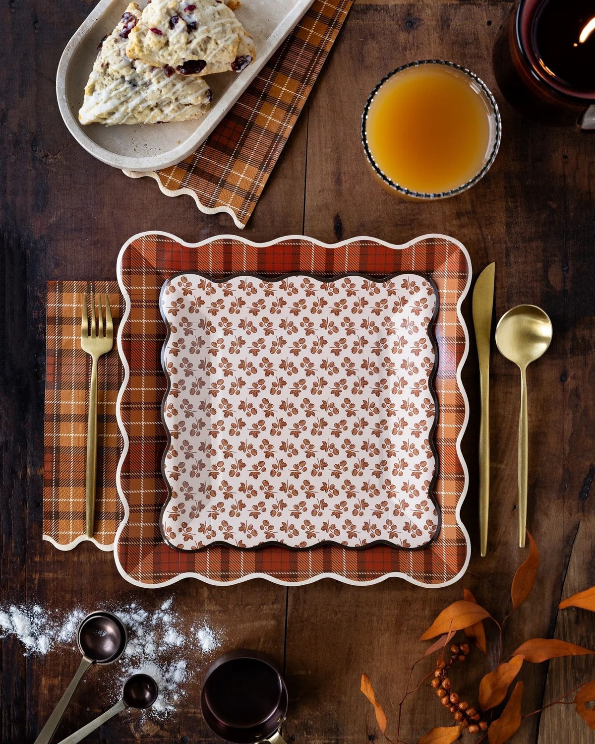Autumn plaid square paper plates with floral fall party plates and coordinating napkins styled on a rustic wooden table with seasonal appetizers and fresh juice for a fall tablescape.