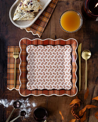 Autumn plaid square paper plates with floral fall party plates and coordinating napkins styled on a rustic wooden table with seasonal appetizers and fresh juice for a fall tablescape.