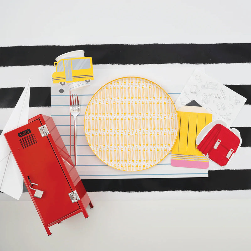 Studio shot of full place setting—empty yellow pencil dinner plate centered on notebook placemat.