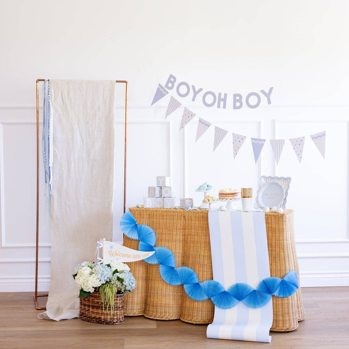 Baby blue baby shower banner and pennant garland styled on wicker table

