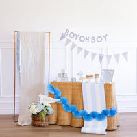 Baby blue baby shower banner and pennant garland styled on wicker table

