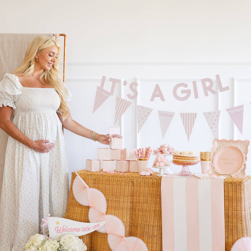 Baby pink banner with “It’s a Girl” lettering styled above a dessert table for a baby shower, featuring soft pink pennants and coordinated party decor.