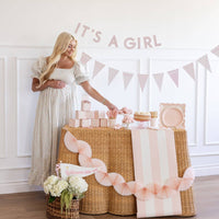 It’s a Girl baby pink banner with matching pink paper pennant banner styled over a baby shower dessert table.