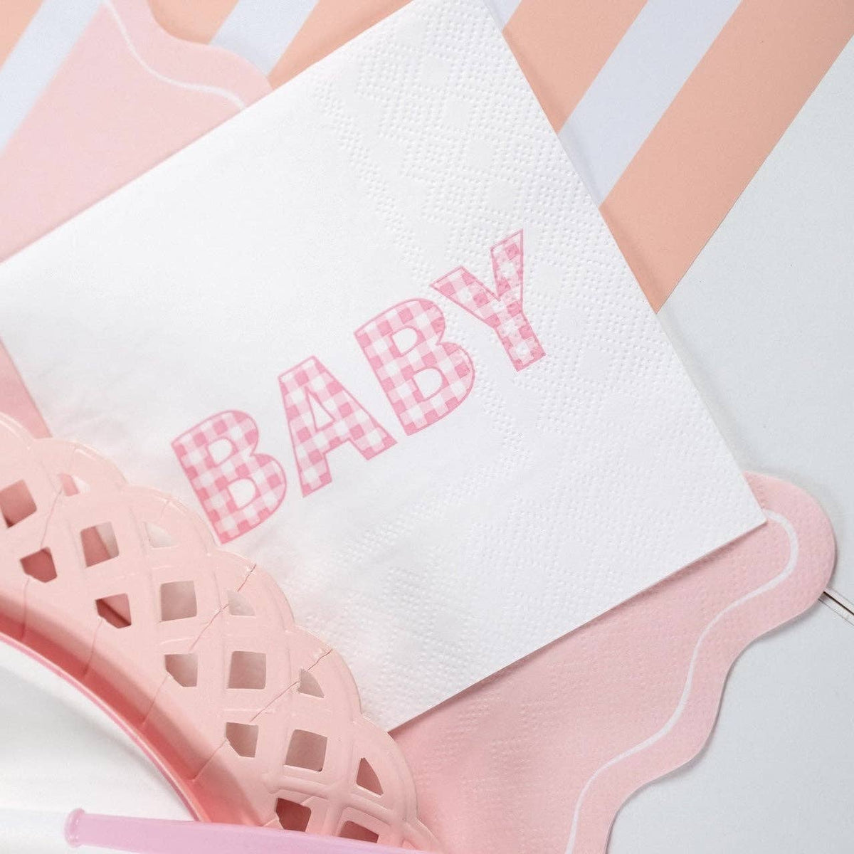Close-up baby shower detail showing a "BABY" napkin beside the pink scalloped napkin on a pink-striped runner.