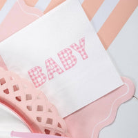 Close-up baby shower detail showing a "BABY" napkin beside the pink scalloped napkin on a pink-striped runner.