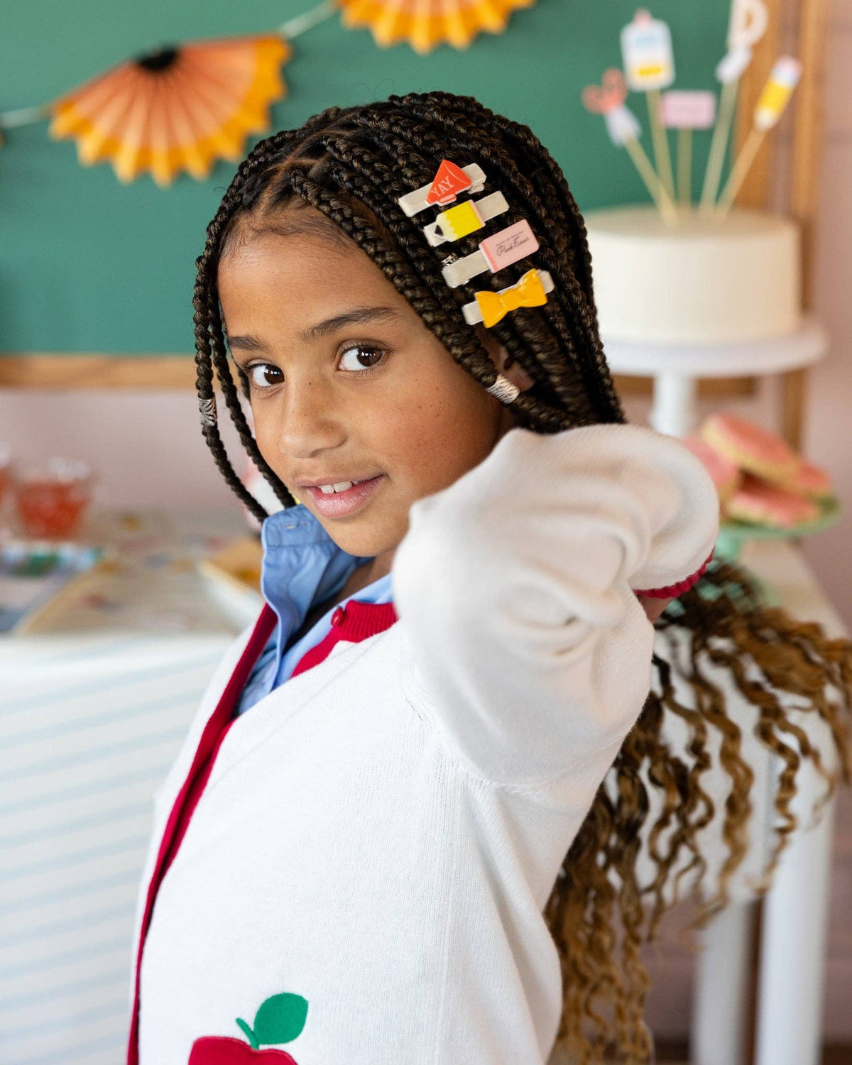 Close-up of young girl with braids wearing four back to school hair clips including YAY megaphone, pencil, pink eraser, and ruler bow