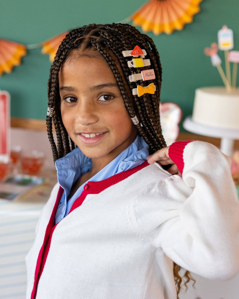 Side profile of young girl with braids wearing back to school hair barrettes including megaphone, pencil, eraser, and ruler bow clips