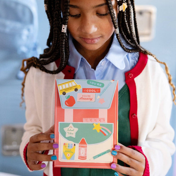 Child holding decorated backpack treat bag with stickers and school icons.
