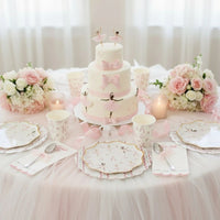 Three-tier white cake decorated with pink bows and ballerina toppers