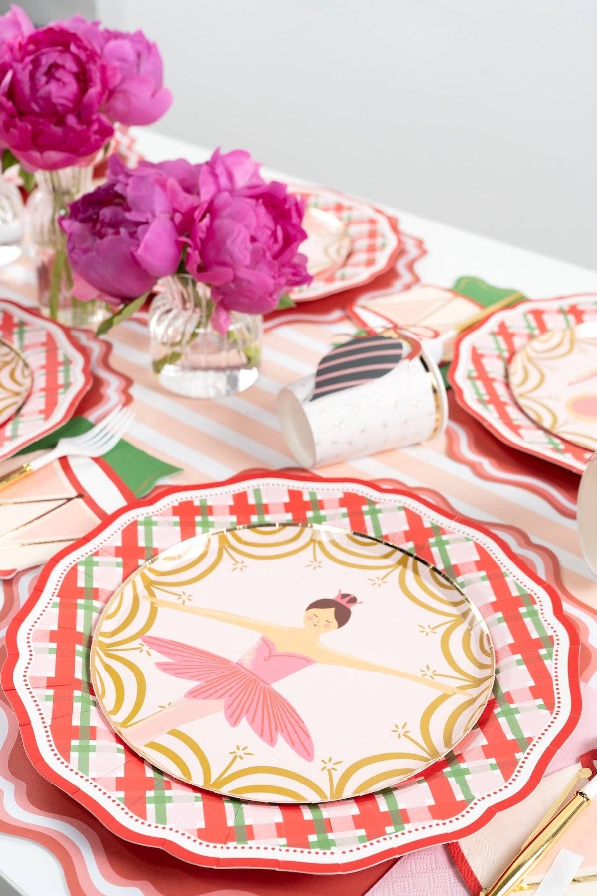 Overhead of ballerina and drum plates on plaid plates with pink peonies and a striped runner.