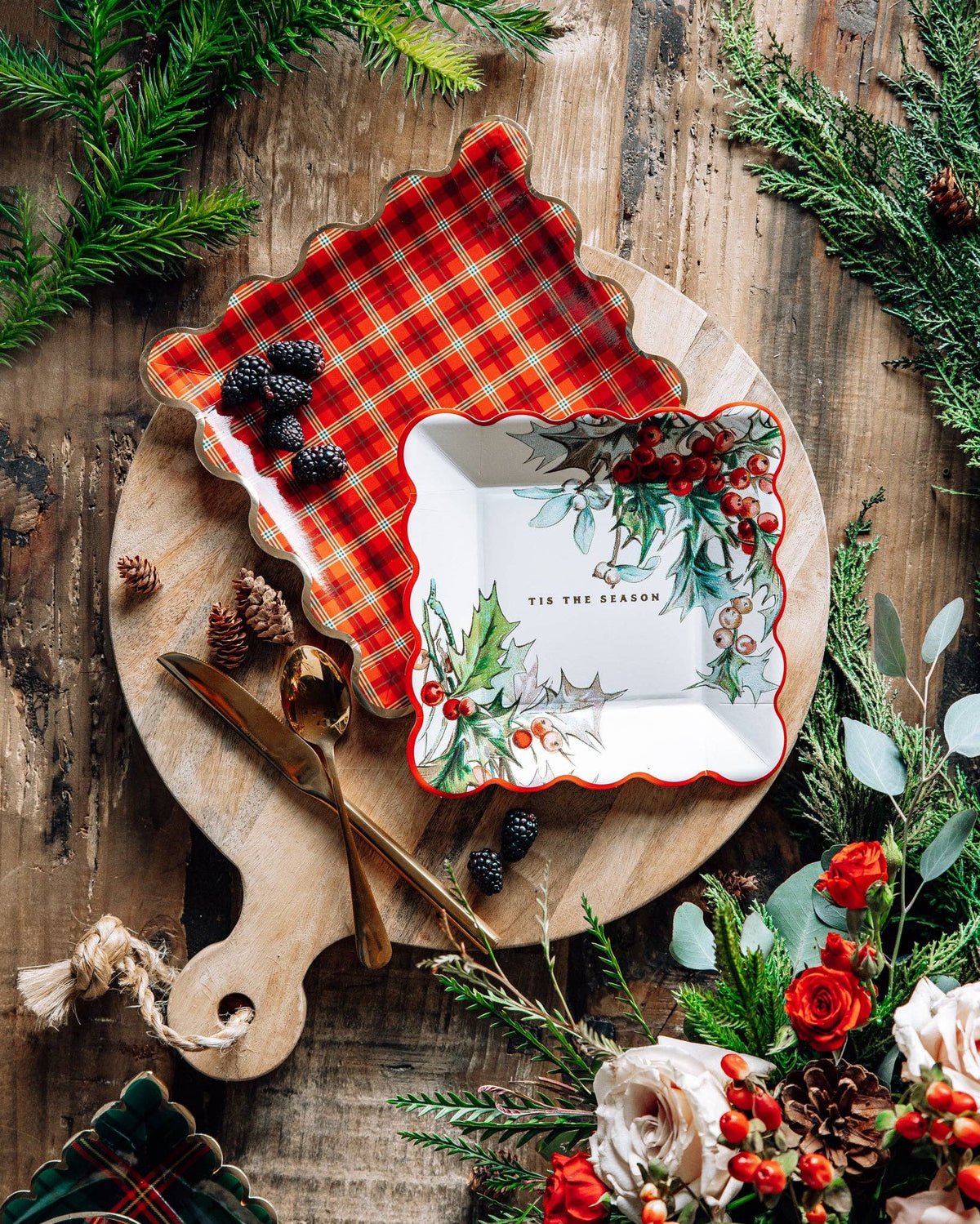 Holiday table setting with holly and red plaid scalloped plates on a wooden board