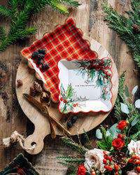Holiday table setting with holly and red plaid scalloped plates on a wooden board