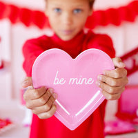 Child holding pink be mine heart shaped paper plate at Valentine party