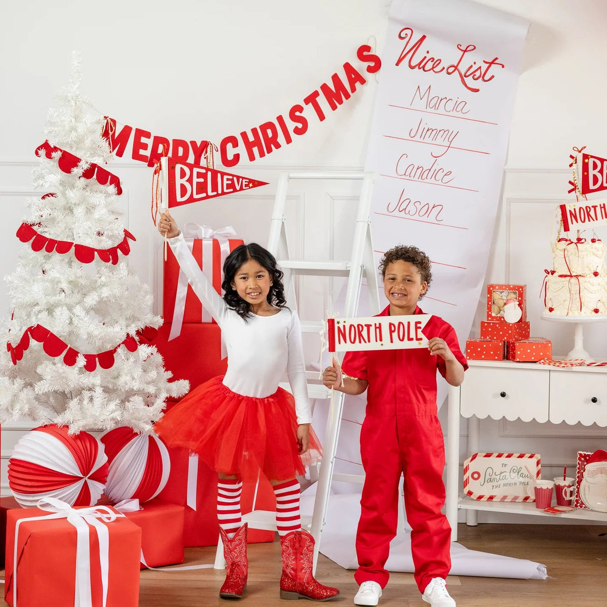 Children posing with Believe and North Pole felt pennant set in front of Christmas tree and party decorations.