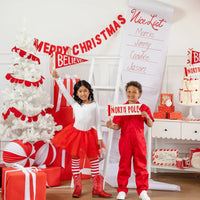 Children posing with Believe and North Pole felt pennant set in front of Christmas tree and party decorations.