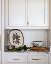 The vintage bell bamboo tray propped on a kitchen shelf with greenery and a bowl.