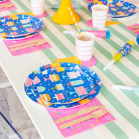 Party table with green stripes, disco balls and pink confetti napkins under bright blue cake-print plates and striped cups.