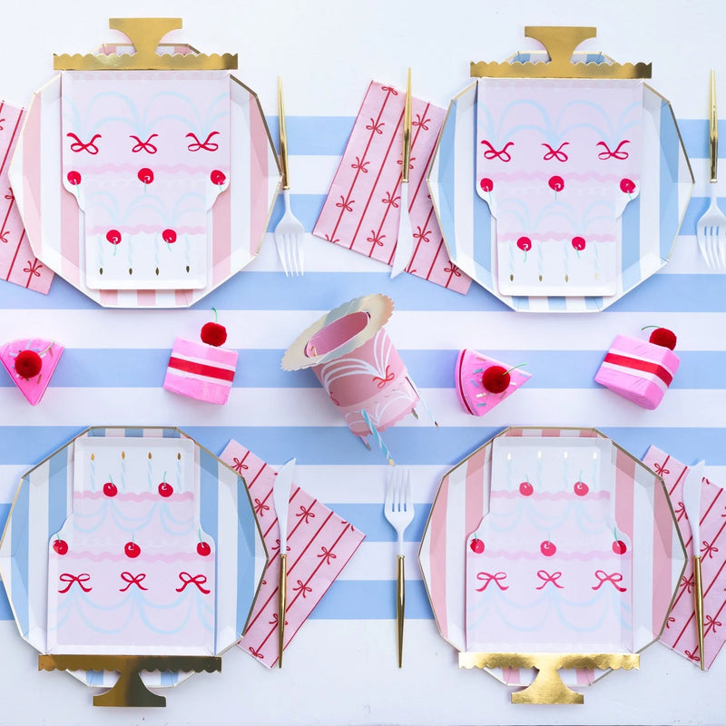 Pink and blue birthday cake place settings arranged on a sky‑blue cabana stripe paper table runner.