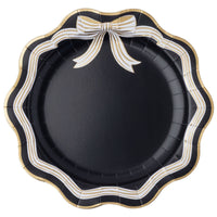 Black bow dinner plate with a black, white, and gold striped scalloped rim and a gold-and-white striped bow at the top, gold-trimmed edge, overhead view on white background.