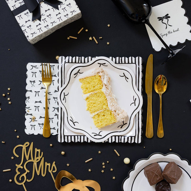 Black Bow Guest Napkin Tablescape with Cake — Black bow guest napkin styled on a black tablescape with cake and gold utensils.