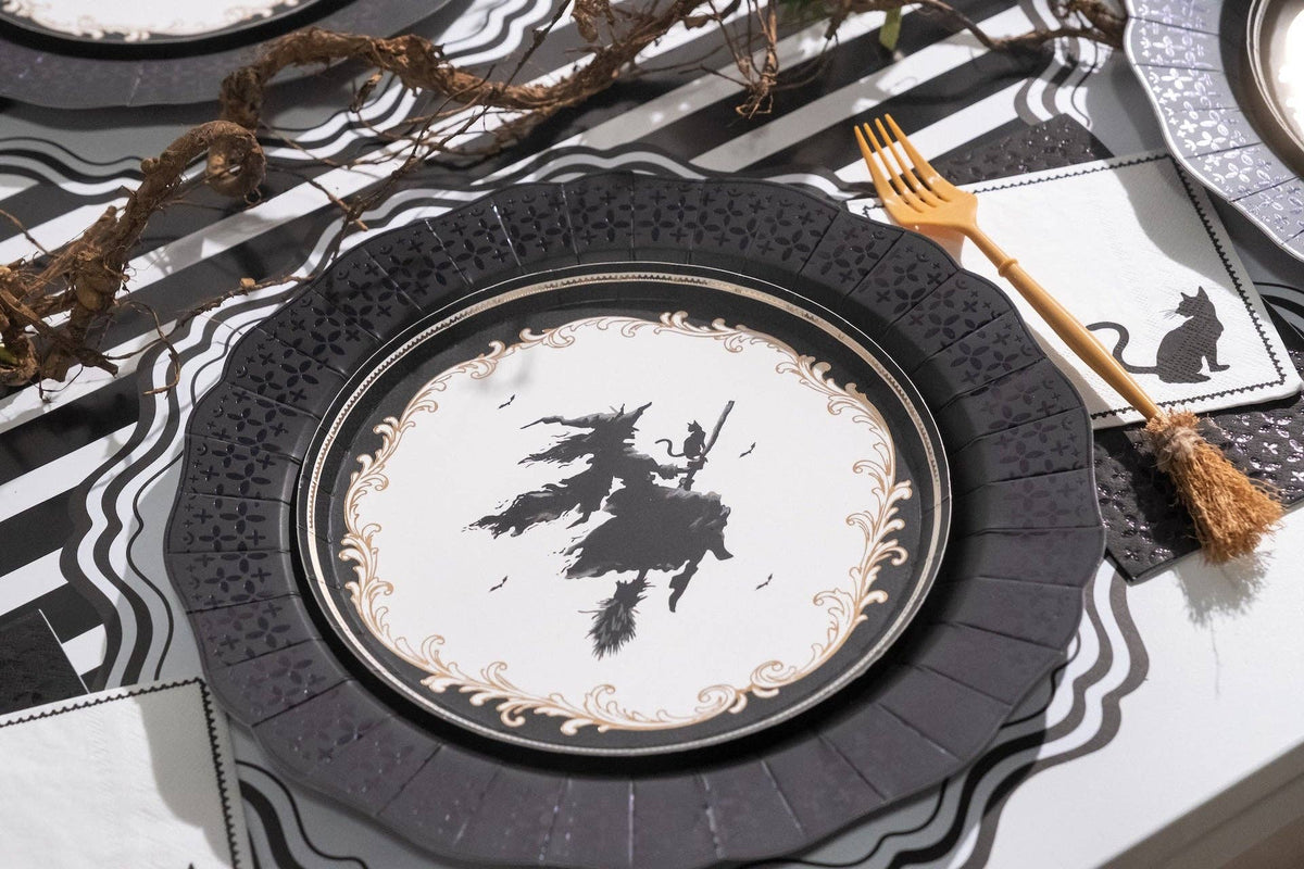 Close up angled place setting highlighting the black cat paper napkin layered on top of a black and white striped table runner.