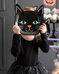 Close-up of the girl holding the black cat plate as a face mask, showing the colorful cat features and holographic glow.