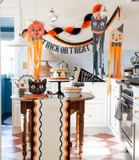 Halloween-themed kitchen with decorations, including a 'Trick or Treat' banner and cat shaped paper plate.