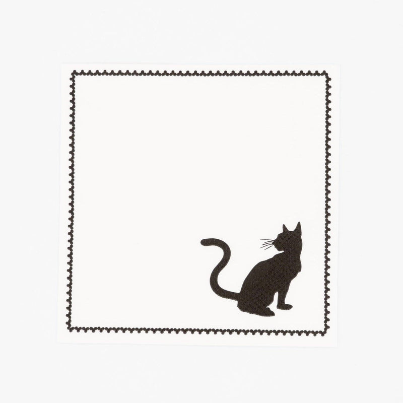 Overhead studio view of a square white paper cocktail napkin featuring a black cat silhouette in the bottom right corner and a printed black stitched border.