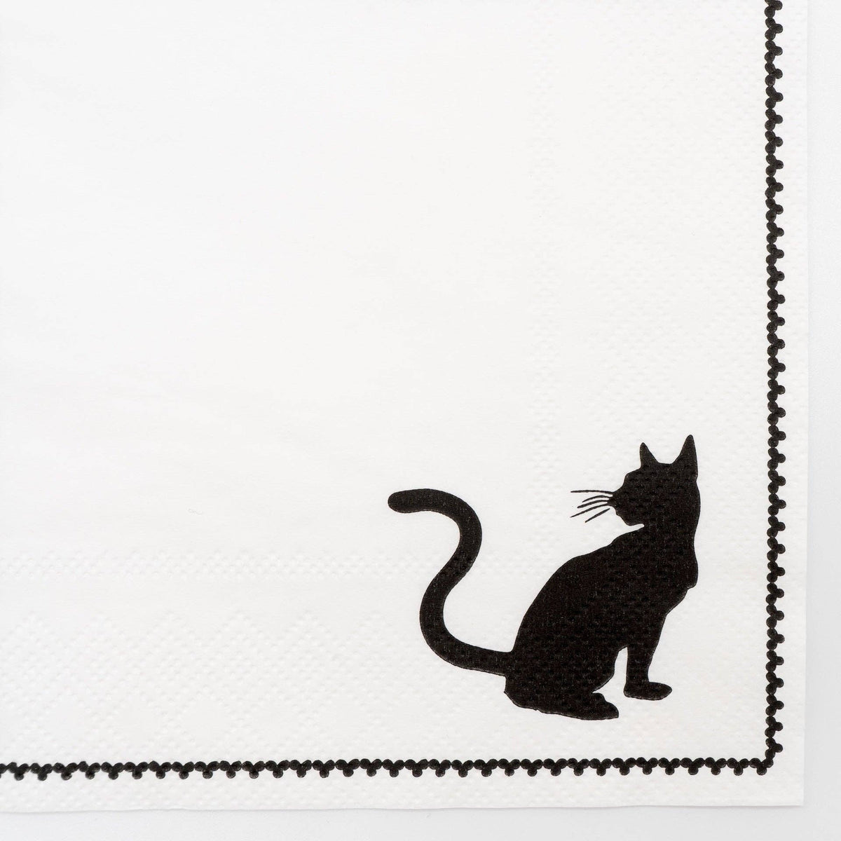 Extreme close up macro detail of the black cat silhouette and the delicate printed picot-stitch edge on the white 3-ply paper napkin.