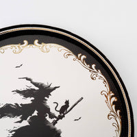 Extreme close up detail highlighting the small black cat sitting on the broomstick of the flying witch silhouette bordered by gold foil.