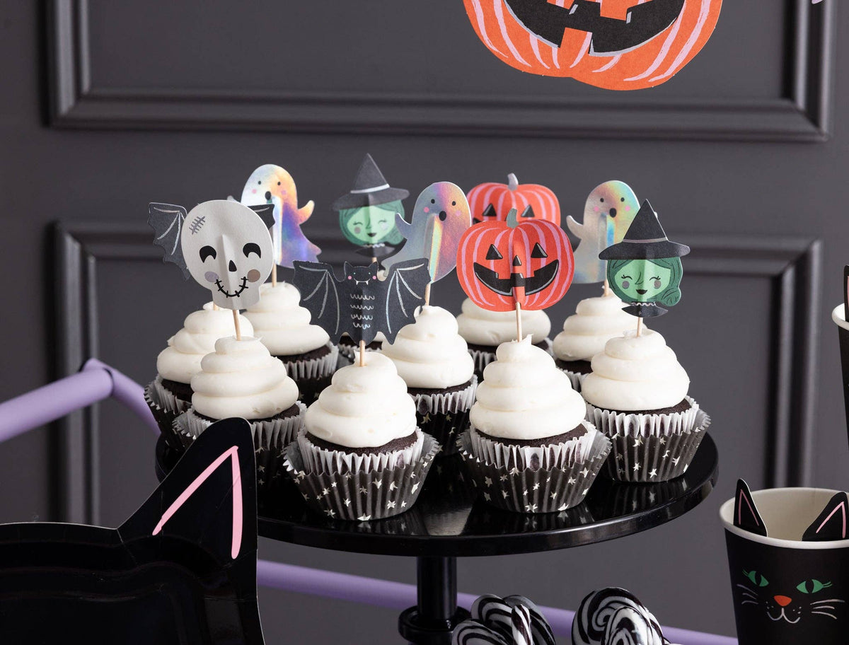 Close up on a tiered black dessert stand filled with frosted cupcakes displaying assorted spooky friends paper toppers.