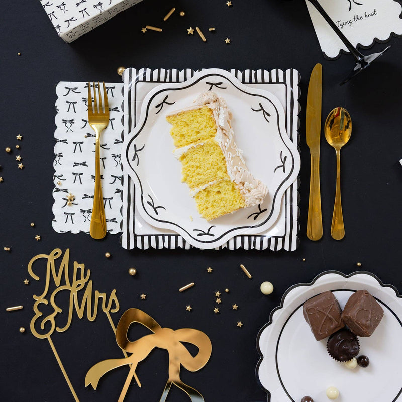 Black and white scalloped plate styled on a black tablescape with gold cutlery, cake slice, and bridal party decorations.