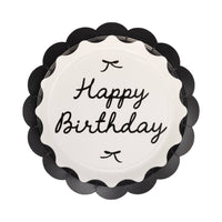 Single round black scalloped paper dinner plate with cream center Happy Birthday cursive script and small bow details on white background