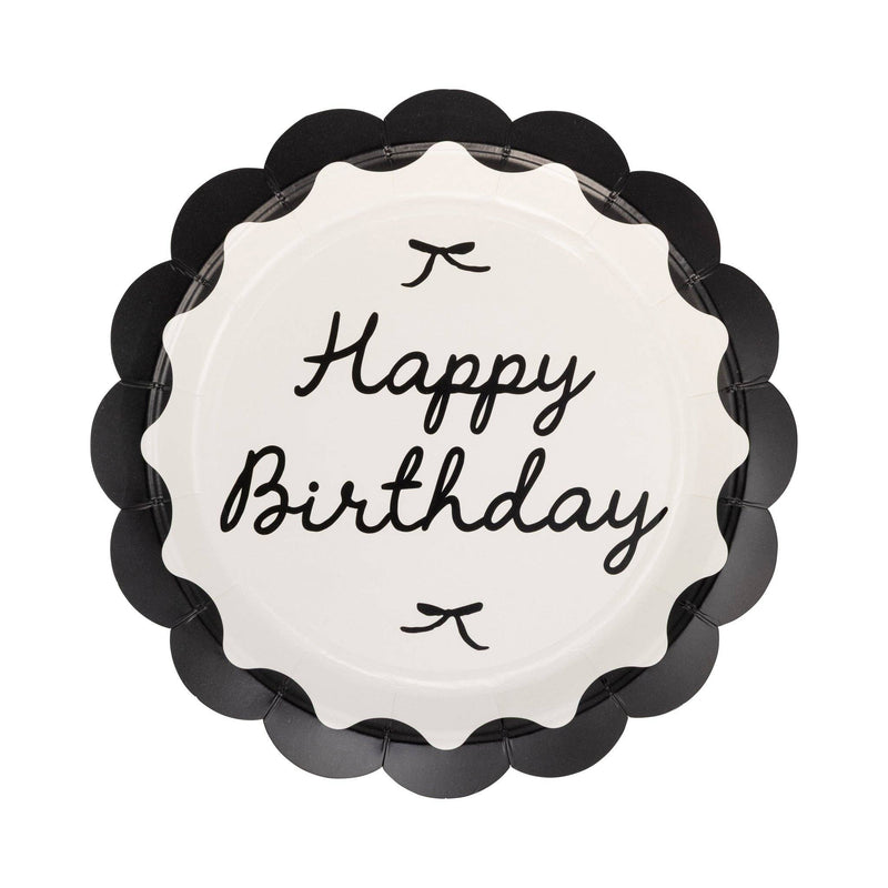 Single round black scalloped paper dinner plate with cream center Happy Birthday cursive script and small bow details on white background