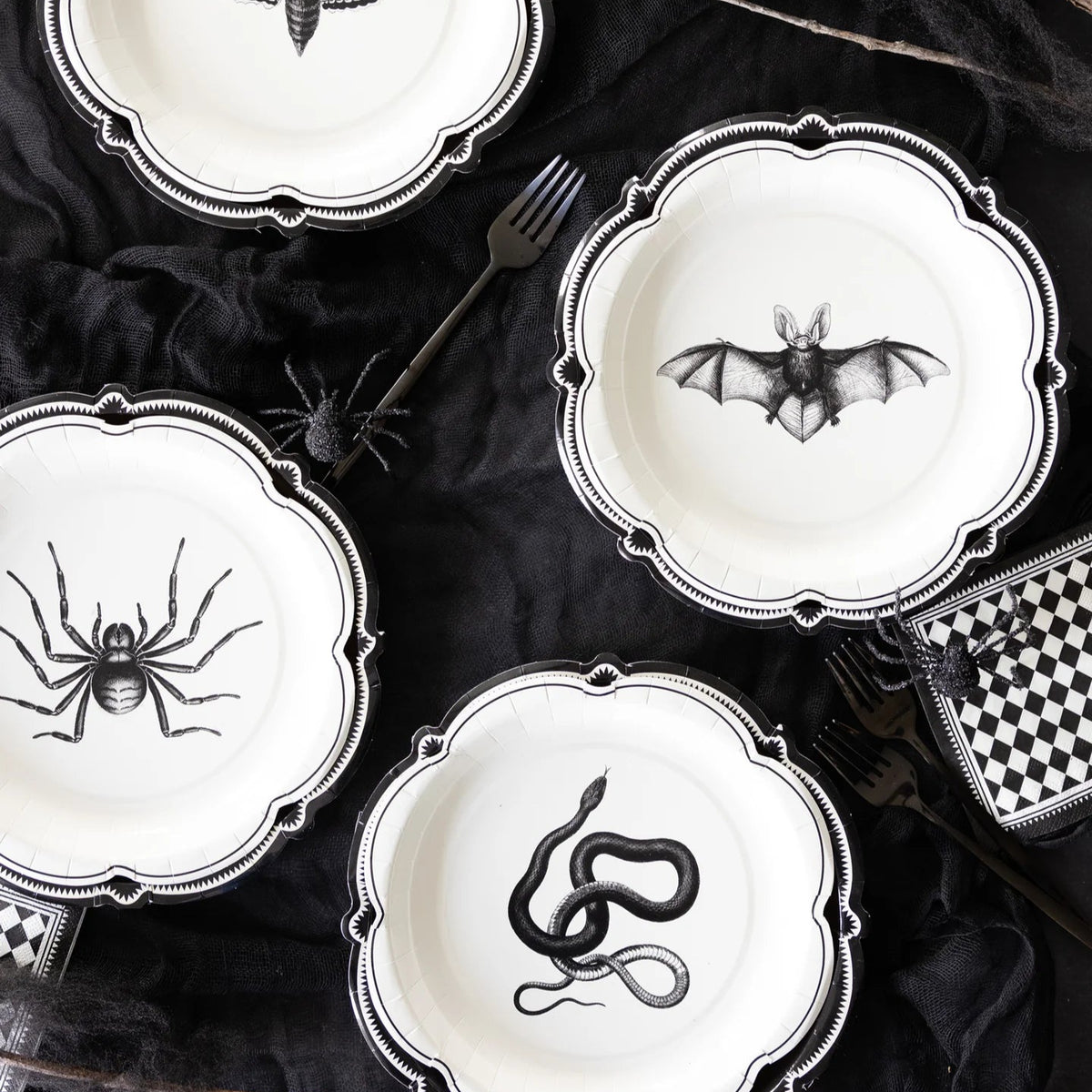 Halloween-themed plates with black spider, bat, and snake designs on a dark surface.