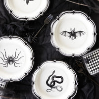 Halloween-themed plates with black spider, bat, and snake designs on a dark surface.