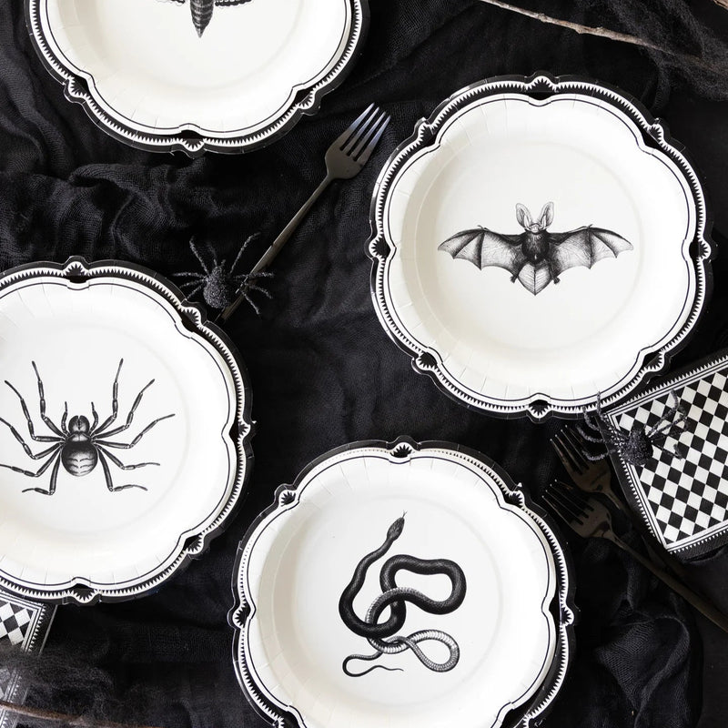 Halloween-themed plates with black spider, bat, and snake designs on a dark surface.