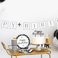 Black and white birthday party bar cart styled with black Happy Birthday scalloped plates, black striped cups, white cake with cake topper and black and white balloon garland
