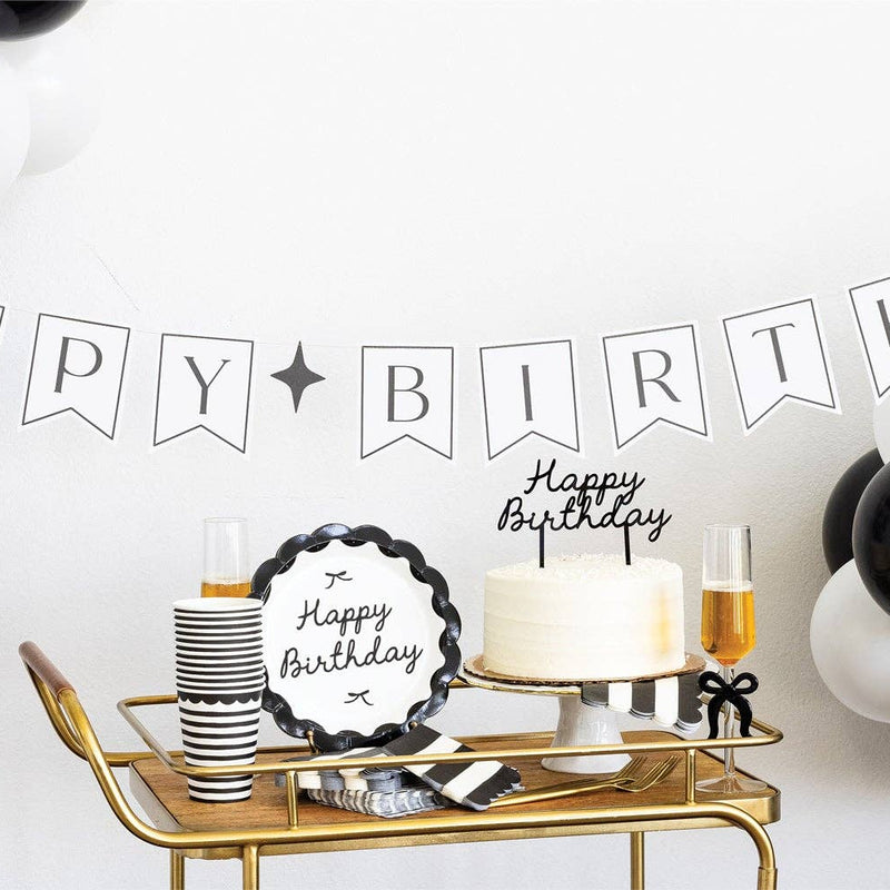 Black and white birthday party bar cart styled with black Happy Birthday scalloped plates, black striped cups, white cake with cake topper and black and white balloon garland