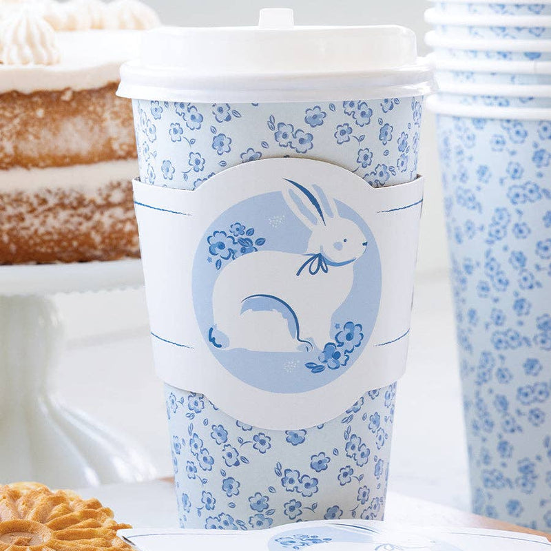 A blue bunny to-go cup styled on a white marble table next to a layered cake and stacks of cups for an elegant Easter or garden party setting.