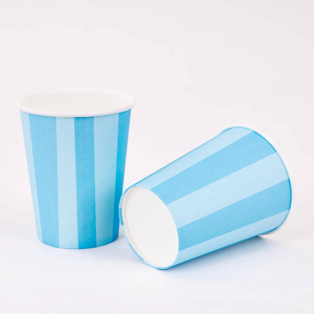 Two blue cabana stripe paper party cups, one upright and one on its side, on a white background.