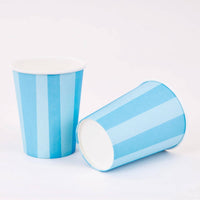 Two blue cabana stripe paper party cups, one upright and one on its side, on a white background.