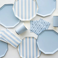 Blue cabana stripe paper plates flat-laid with solid sky blue plates, blue striped napkins, and blue bow-print cocktail napkins from the coordinating blue collection