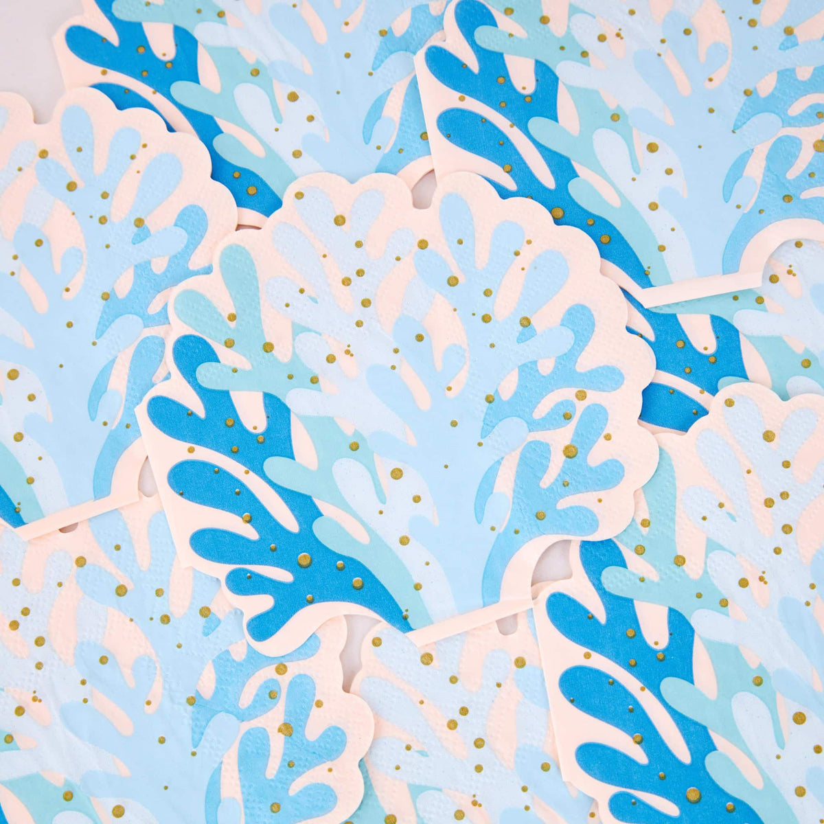 Overlapping blue coral shaped napkins with layered blue tones, blush edges, and gold foil dots.