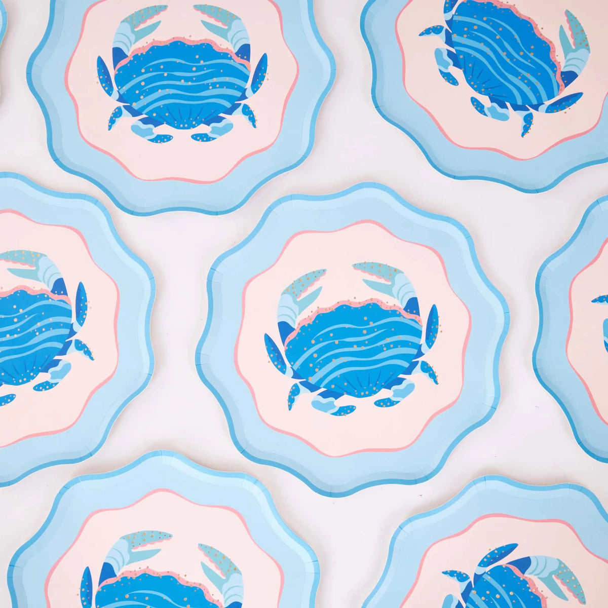 A repeating grid of the scalloped blue crab plates on white, showing the consistent crab illustration and wavy layered edge. Pattern product shot.