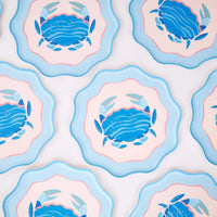 A repeating grid of the scalloped blue crab plates on white, showing the consistent crab illustration and wavy layered edge. Pattern product shot.
