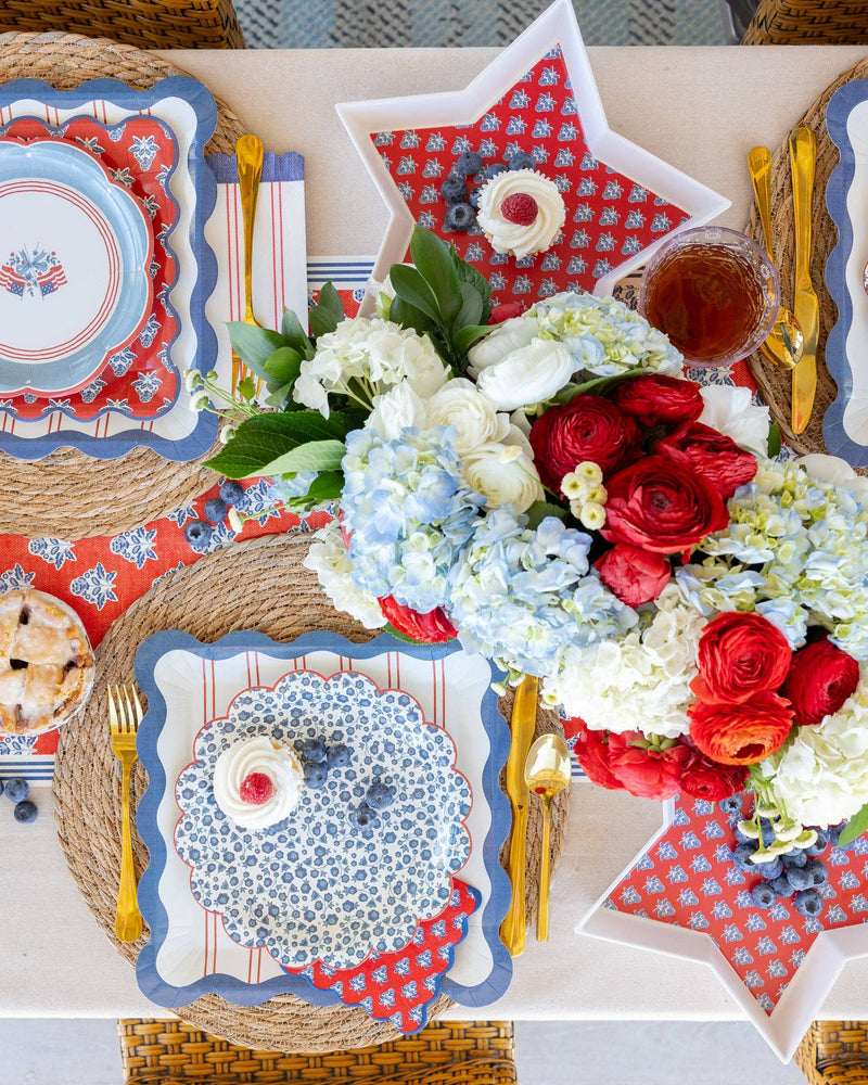 Blue ditsy floral plates in full Hamptons red, white, and blue tablescape overhead with red striped dinner plates, red block-print napkins, star trays, hydrangeas, and gold cutlery